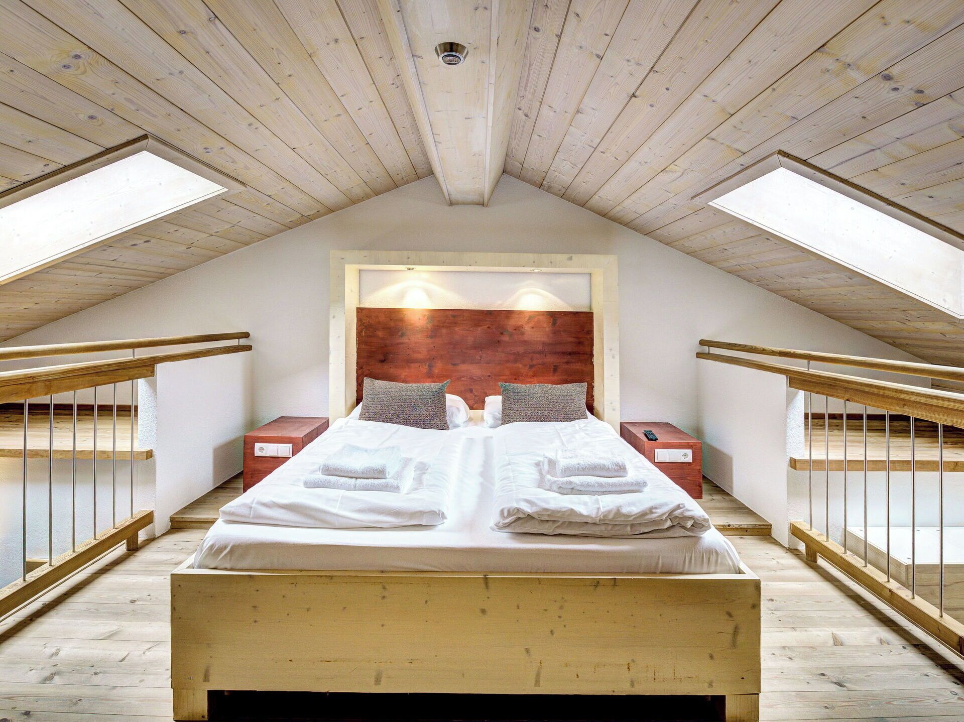 Een slaapkamer met een houten plafond, een groot bed met witte lakens, twee nachtkastjes en een houten hoofdbord.