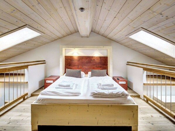 A bedroom with a wooden ceiling, a large bed with white linens, two nightstands, and a wooden headboard.