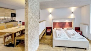 A bedroom with a wooden headboard, a white bed, and a dining area with a wooden table and chairs.