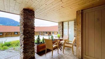 A wooden ceiling, stone pillar, wicker chairs, a table, and a view of buildings and mountains.