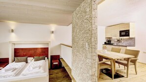 Quarto com cama, mesas de cabeceira, painel de cabeceira de madeira, parede divisória de pedra, área de jantar com mesa e cadeiras e cozinha com micro-ondas.
