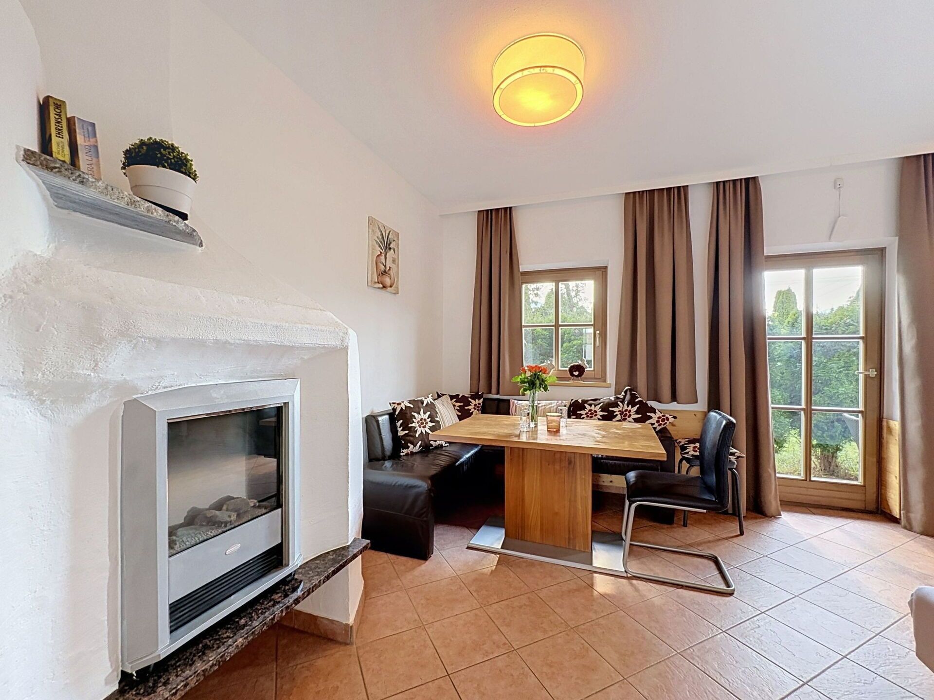 A living room with a fireplace, a dining table with chairs, and a large window with curtains.