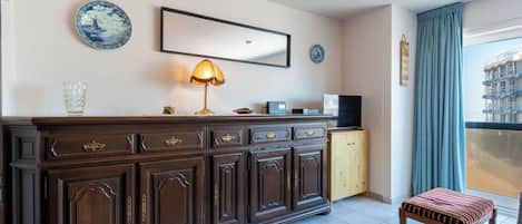 A hotel room with a wooden cabinet, a television, a lamp, and a view of a building through the window.