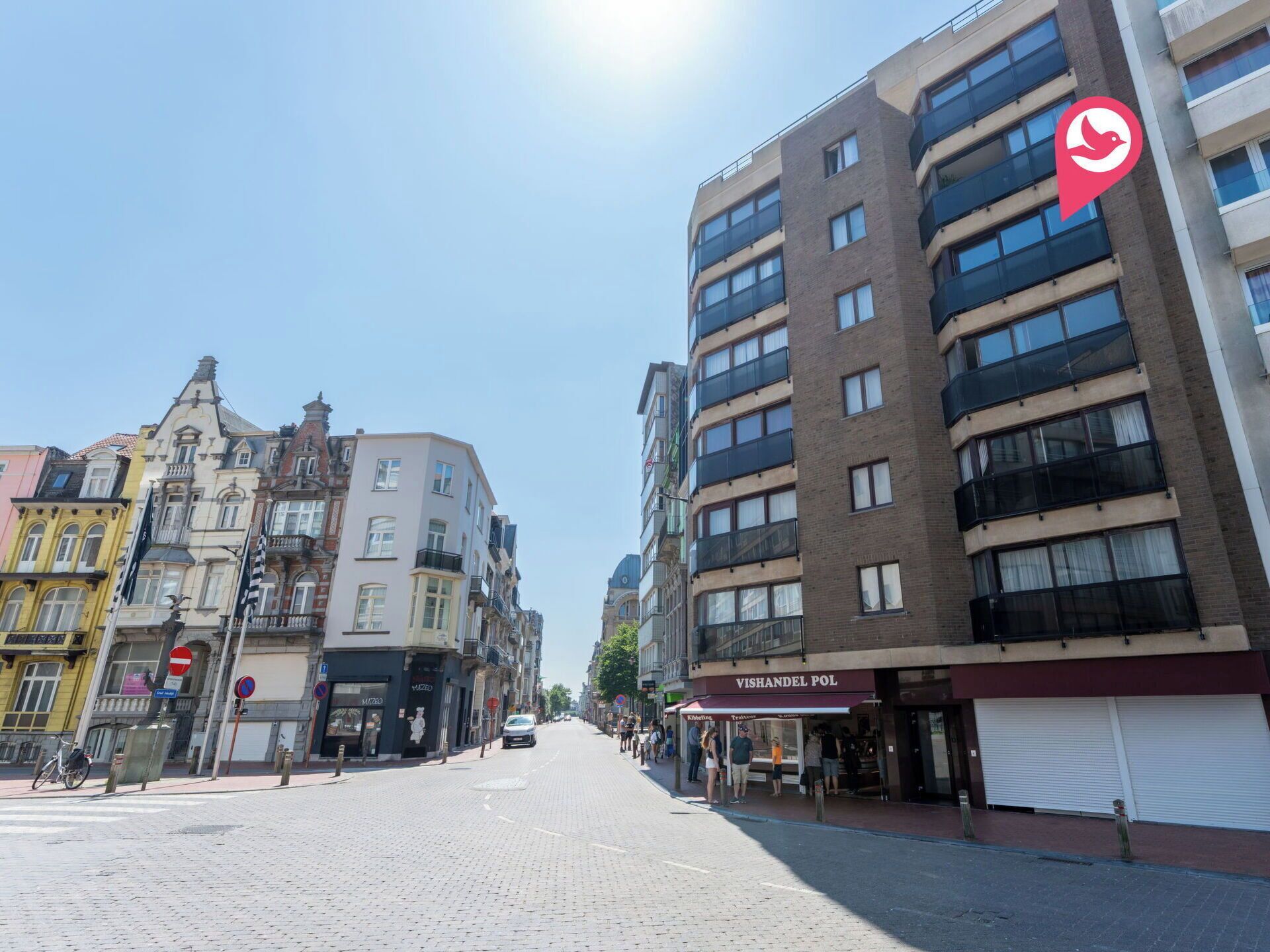 Een straat met gebouwen, waaronder een modern gebouw met een bord voor 'VISHANDEL POL'.