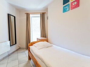Ein kleines, sauberes Zimmer mit einem Einzelbett, einem Nachttisch, einem Spiegel und einem Fenster mit Vorhängen.