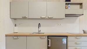 Kompakti keittiö, jossa on astianpesukone, moderni hana ja allas sekä pieni hylly, jossa on pullo ja säilytysastia.