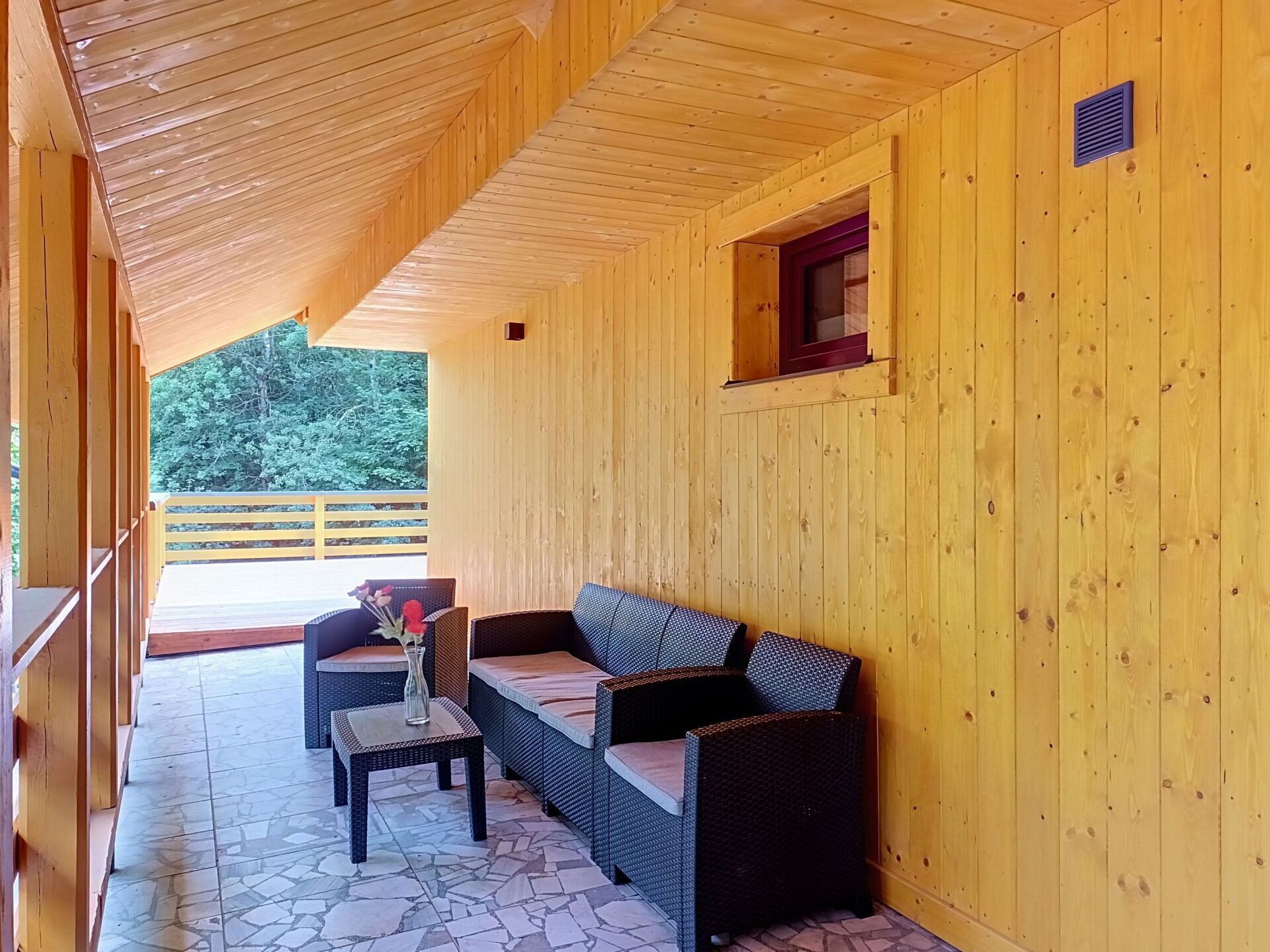 Een houten hutje met een overdekte veranda, rieten meubilair en een vloer van natuursteen.