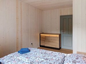 Una habitación con paredes de madera, una cama con ropa de cama floral, un aparador de madera y una puerta.