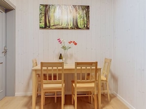 Ein Essbereich mit einem Holztisch und Stühlen, einem Waldgemälde und einer Vase mit Blumen.