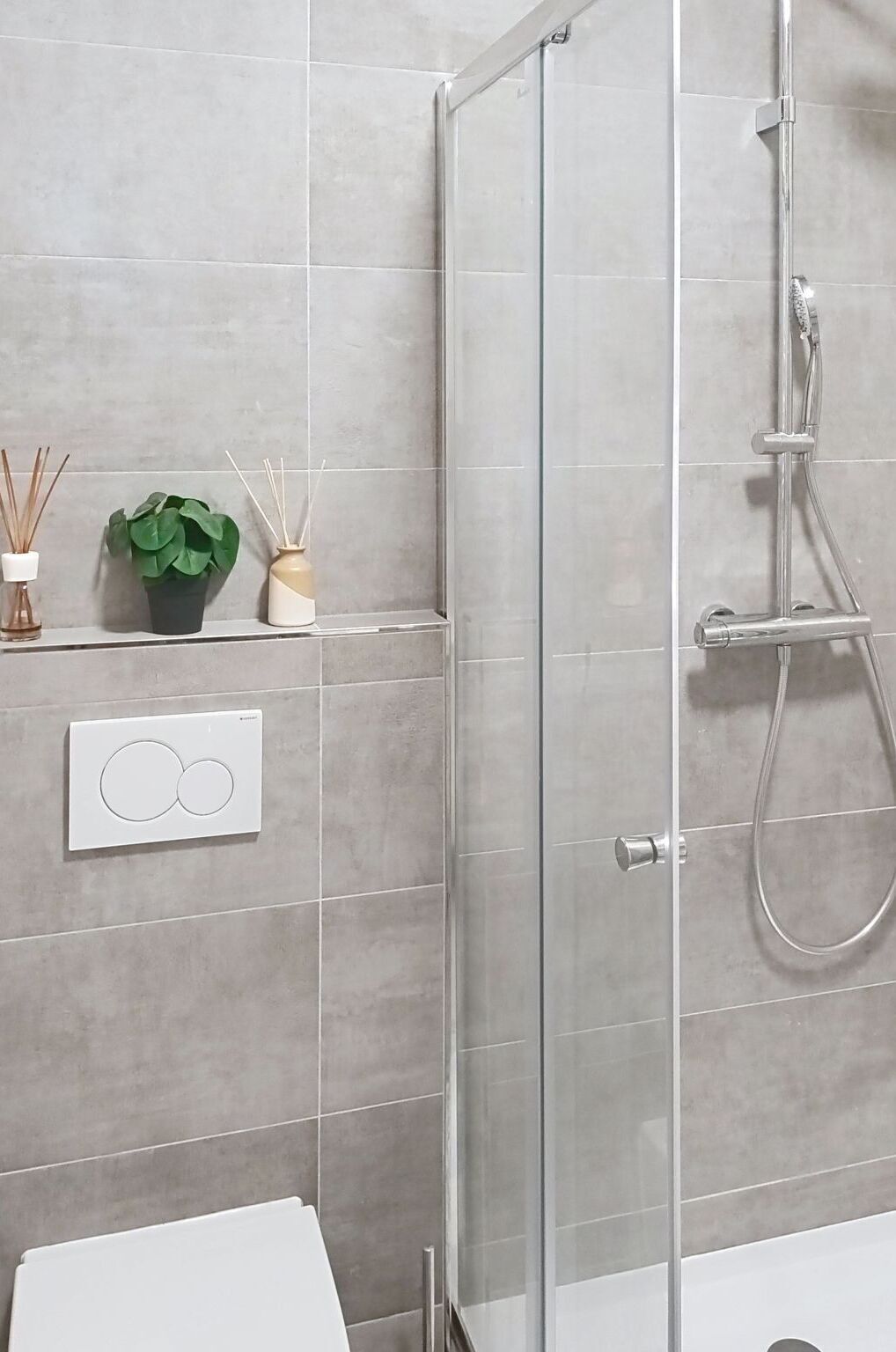 Een moderne badkamer met een douchecabine van glas, een toilet en een bedieningspaneel aan de muur.