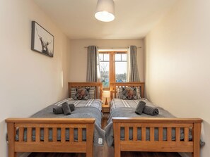 Ein Zimmer mit zwei Holzbetten, einem Vorhangfenster, einer Lampe und einem gerahmten Bild an der Wand.