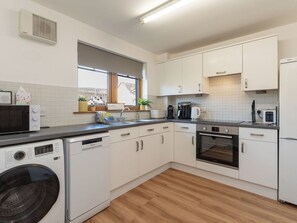 Eine moderne Küche mit weißen Schränken, einem integrierten Geschirrspüler, einer Waschmaschine, einer Kaffeemaschine und einem Backofen.