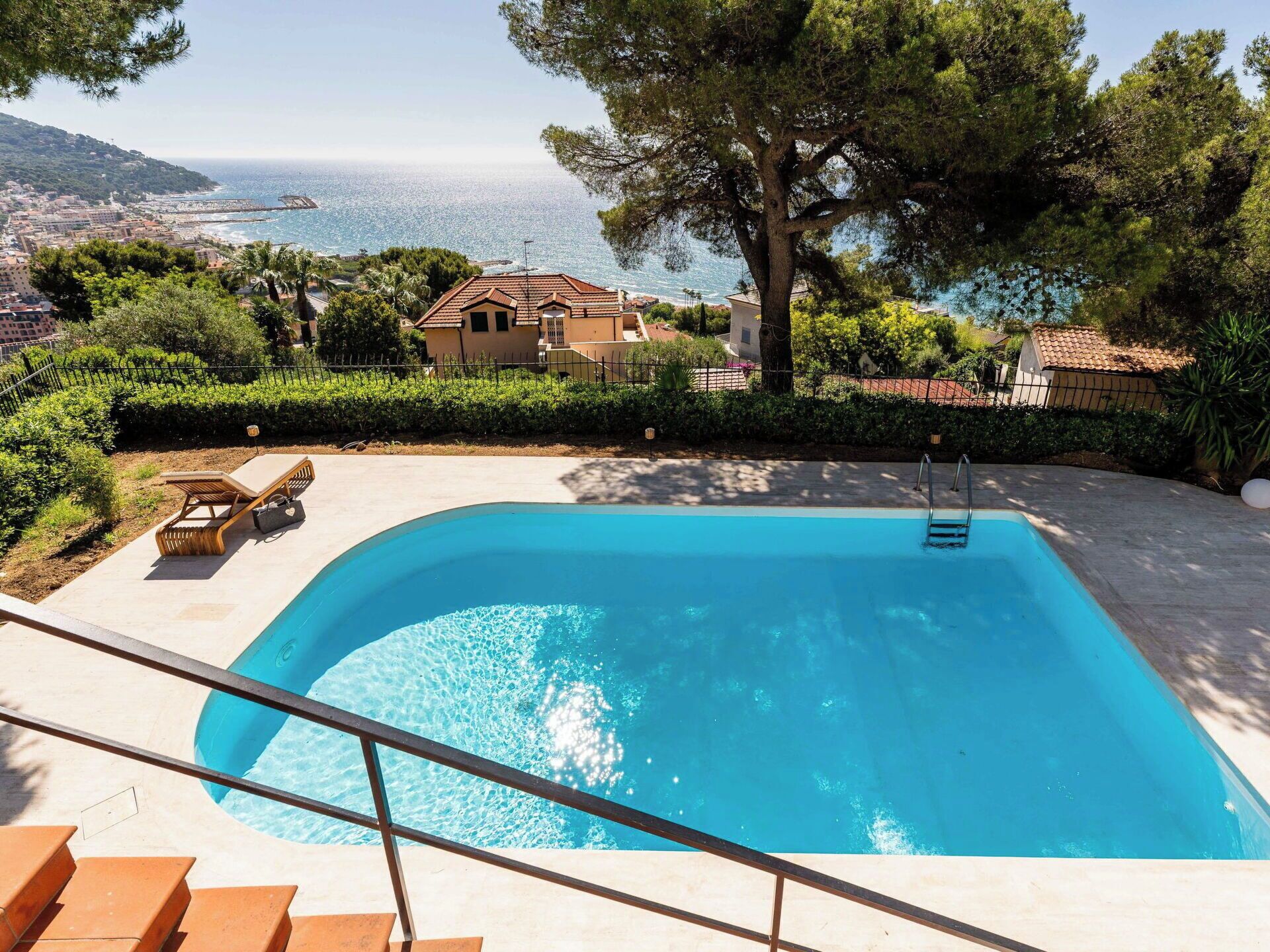 A swimming pool with a view of the sea, surrounded by greenery and a house.