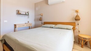 Ein Schlafzimmer mit einem Bett, Nachttischlampen, einer Wand-Klimaanlage, einem Nachttisch und einem kleinen Hocker.