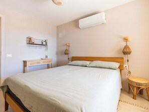 Ett sovrum med en säng, sänglampor, en väggmonterad luftkonditioneringsanläggning, ett sängbord och en liten pall.