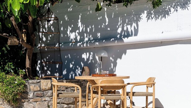 Ein Außenbereich mit Tisch und Stühlen, einer Steinsäule und einem Baum, der Schatten spendet.