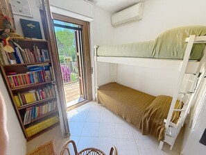 Ein Zimmer mit einem Etagenbett, einem Bücherregal und einem Fenster mit Blick auf Grünflächen.