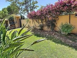 Ein Garten mit einer gelben Mauer, grünem Gras und blühenden rosa Pflanzen.