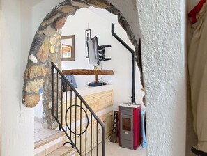 Ein Zimmer mit einem steinernen Bogen, einem Holztisch, einem roten Heizkörper und einer schwarzen Rohrleitung.