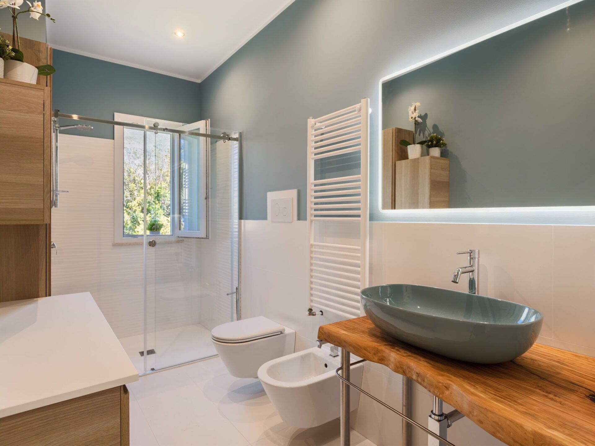 Un baño moderno con cabina de ducha de vidrio, inodoro blanco, bidé, lavamanos grande tipo recipiente y encimera de madera.