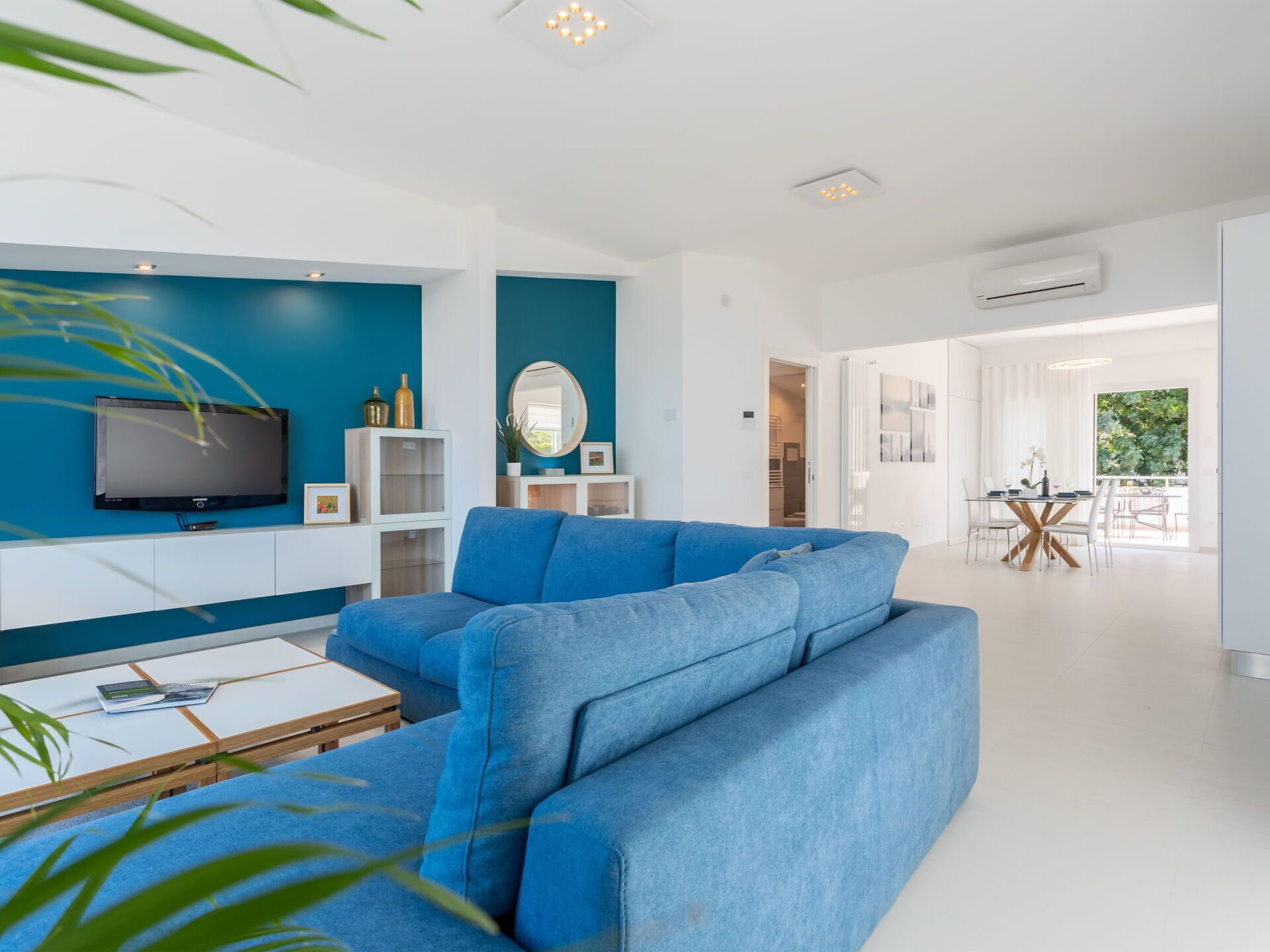 A modern living room with a sectional sofa, a flat-screen TV, and a dining area with a table and chairs.