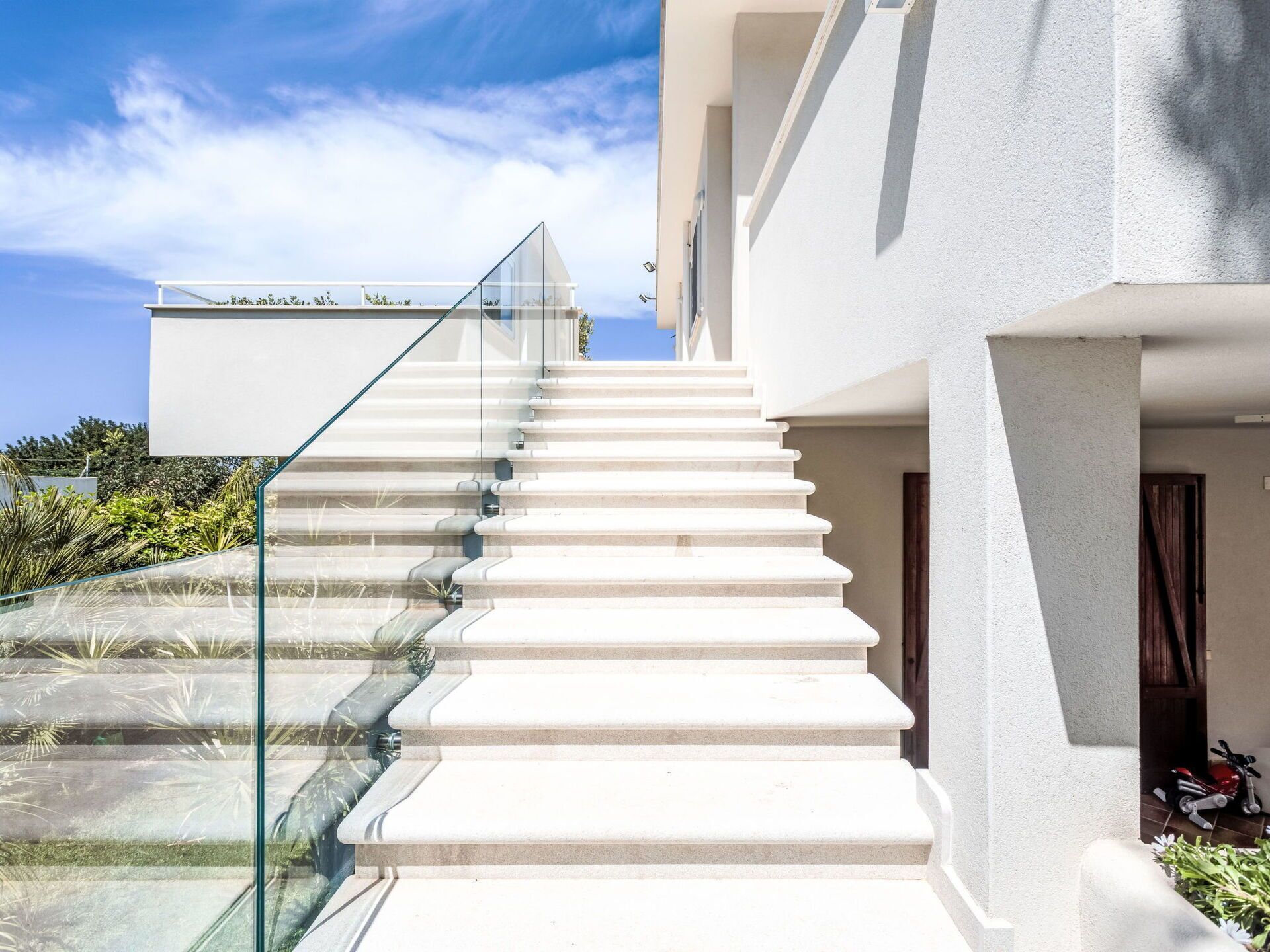 A modern staircase with glass railings leading to a white building.