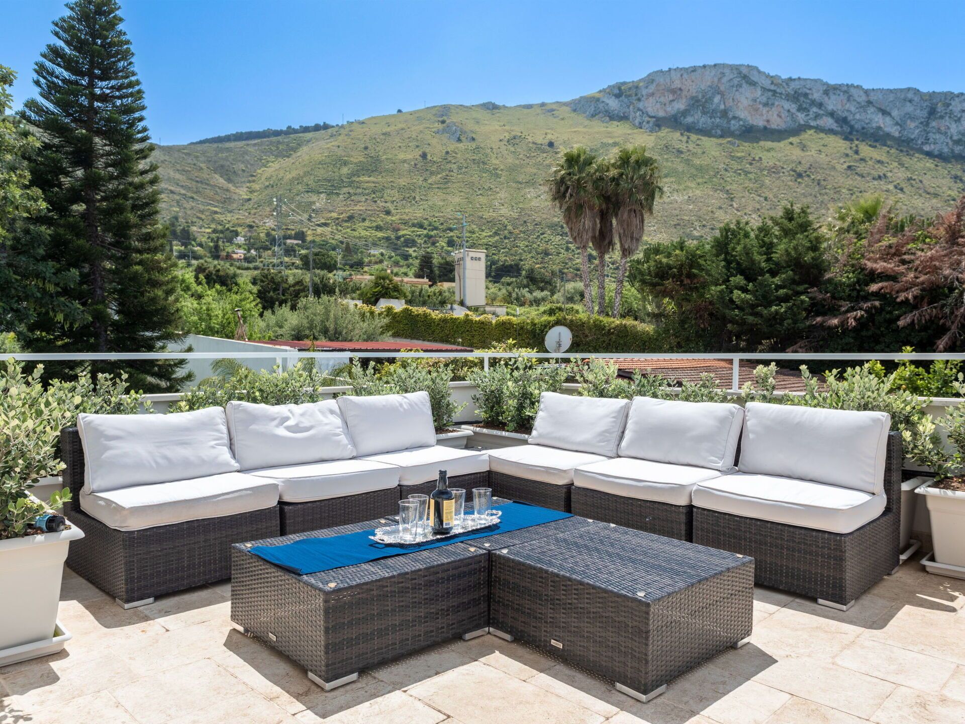 Une terrasse dotée d’un canapé modulable et d’une table basse, entourée de plantes en pot et offrant une vue sur un paysage montagneux.