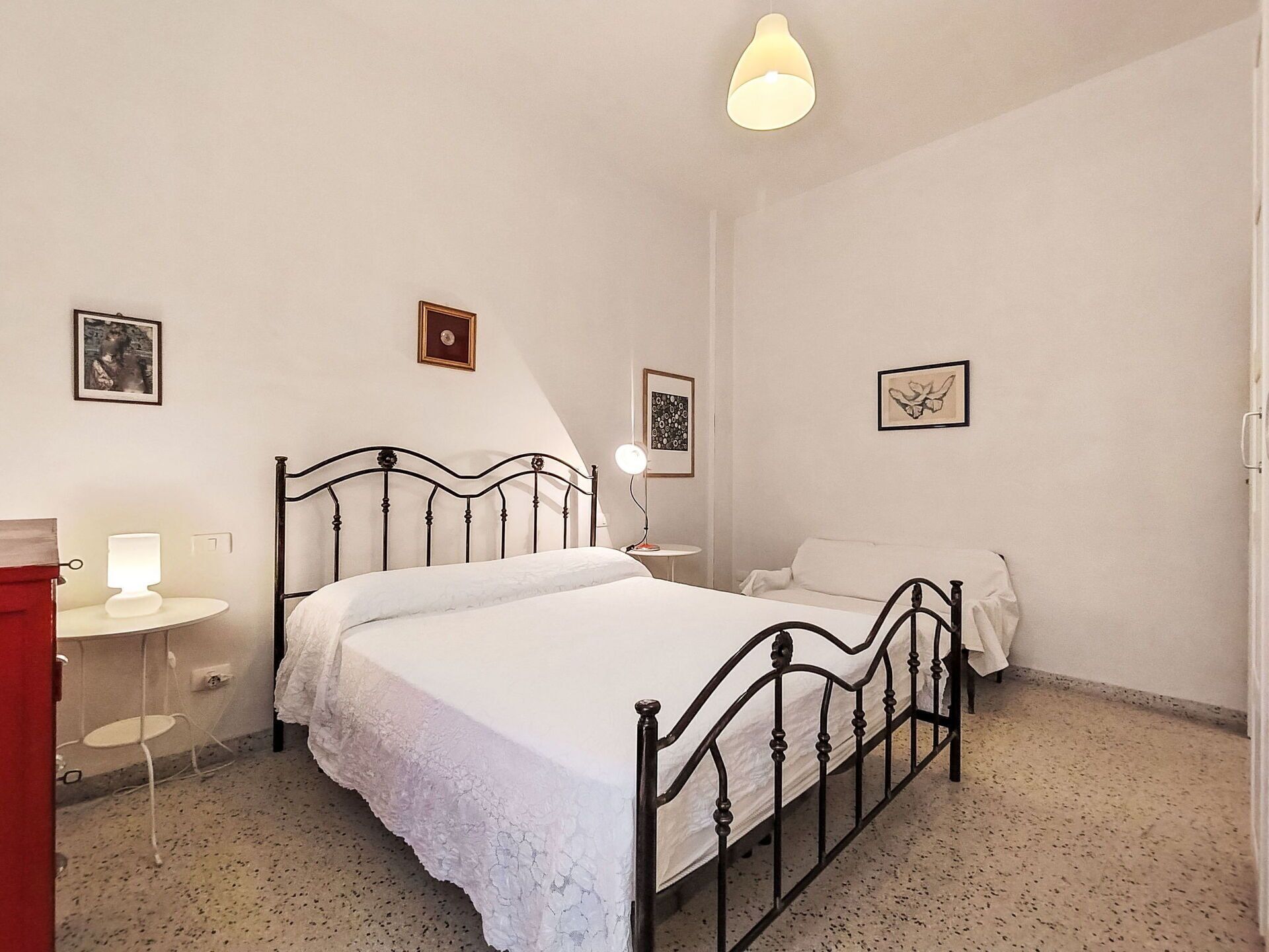 Ein Schlafzimmer mit einem Bett, Nachttischen, einer Lampe und gerahmten Bildern an den Wänden.