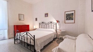 Um quarto com cama, mesa de cabeceira, abajur e um aparador vermelho.