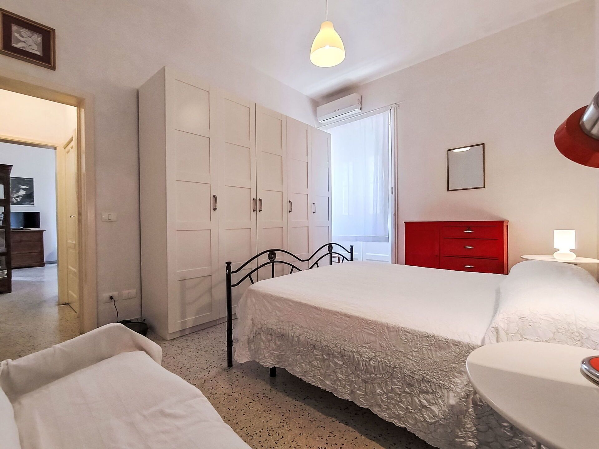 Un dormitorio con una cama, un armario, un aparador rojo y una ventana.