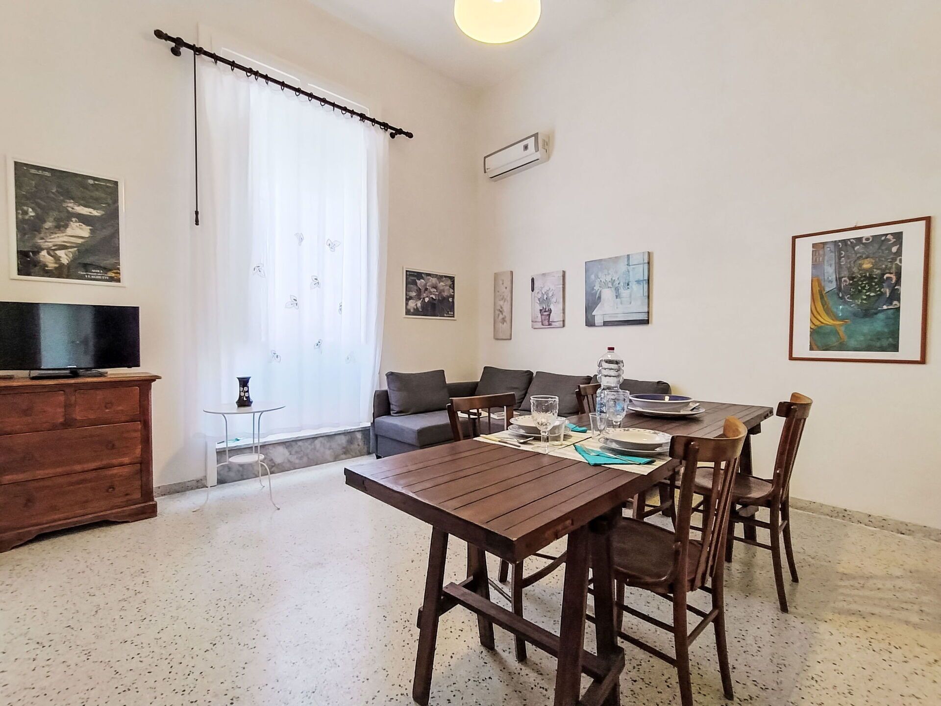 Un'area pranzo con un tavolo e sedie in legno, un divano, una TV e opere d'arte alle pareti.