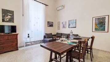 Un'area pranzo con un tavolo e sedie in legno, un divano, una TV e opere d'arte alle pareti.