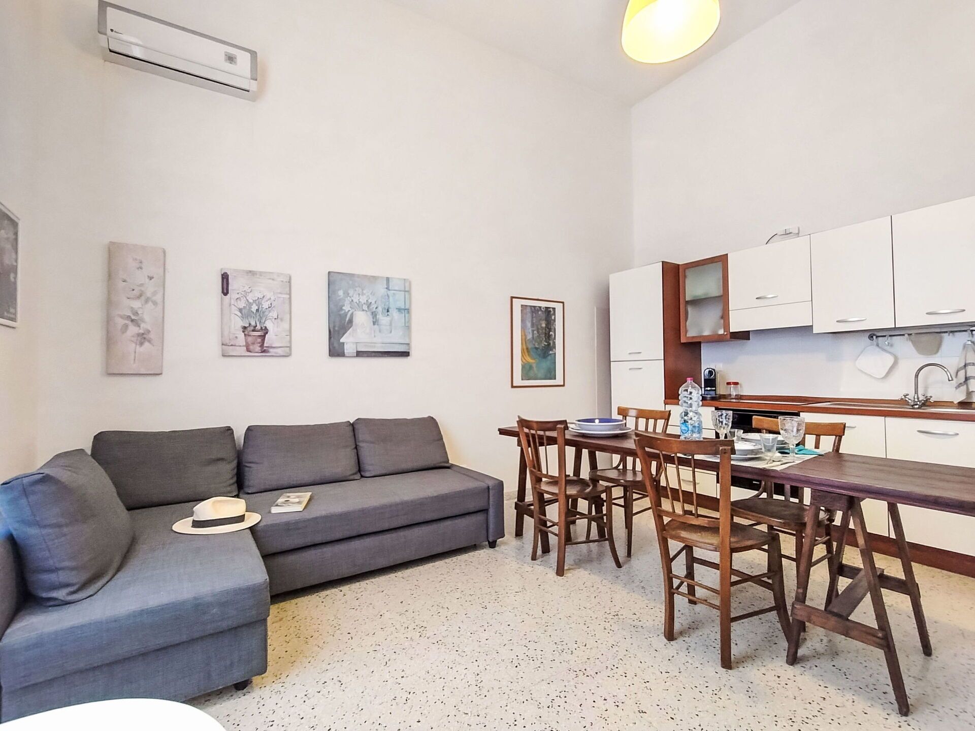 Un espacio habitable compacto con un sofá gris, una mesa de comedor con sillas, una zona de cocina y obras de arte colgadas en la pared.