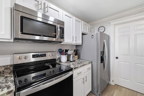 A modern kitchen with stainless steel appliances, white cabinetry, and a marble countertop. - The Beach Club 104C by Liquid Life (Gulf Shores)