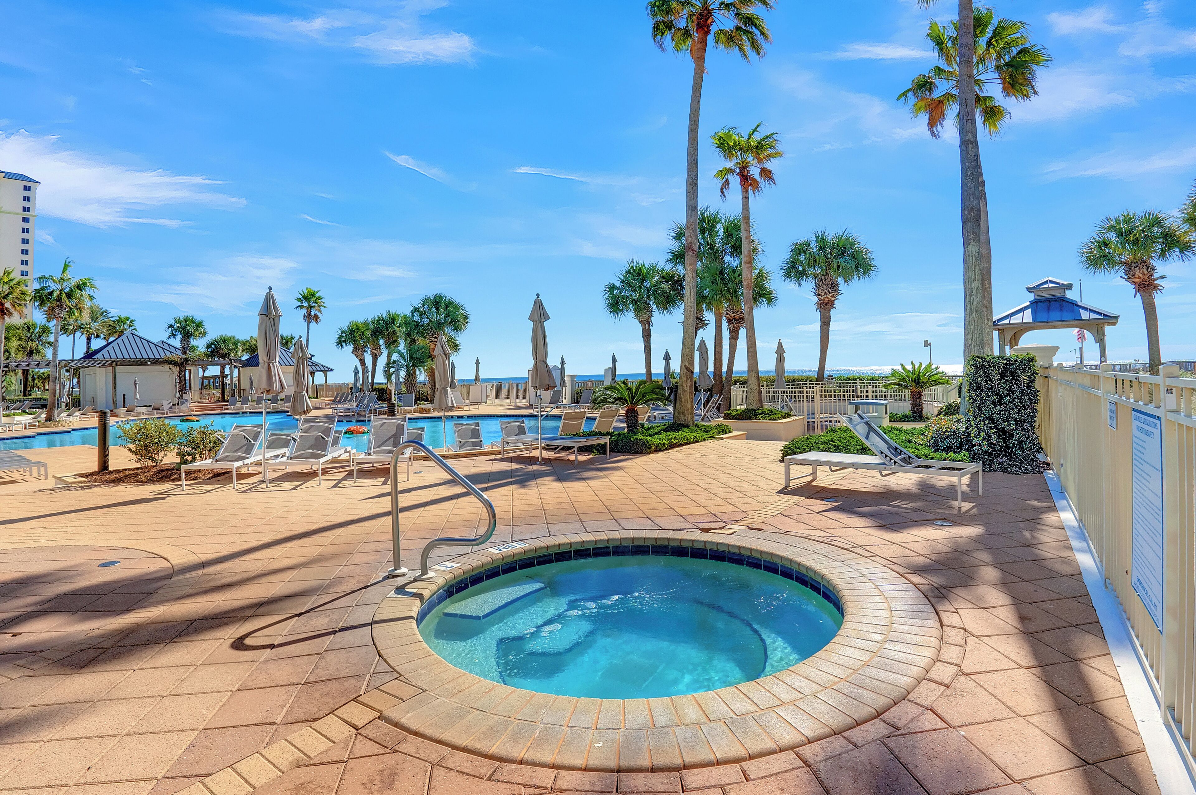 Un espace piscine avec des chaises longues, un jacuzzi et des palmiers.