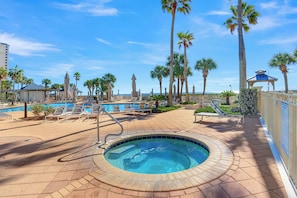 A pool area with lounge chairs, a hot tub, and palm trees. - The Beach Club 104C by Liquid Life (Gulf Shores)