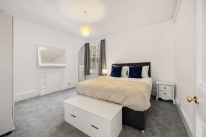 A bedroom with a bed, bedside table, nightstand, dresser, mirror, and a window with curtains. - Great Titchfield Street 1Bed 1Bath in the heart of London. Newly refurnished (London)