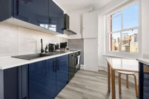 A modern kitchen with dark blue cabinets, a white countertop, and a view of buildings through a large window. - Great Titchfield Street 1Bed 1Bath in the heart of London. Newly refurnished (London)
