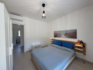 Ein modernes Schlafzimmer mit einem großen Bett, einem Nachttisch, einem Wandregal und einer Deckenleuchte.