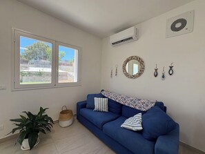 Une pièce avec un canapé bleu, une plante en pot, un climatiseur fixé au mur, une fenêtre donnant sur un beau paysage et un miroir décoratif.
