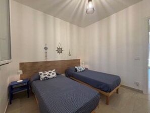 Ein Schlafzimmer mit zwei Betten, einem Holzkopfteil, einem Nachttisch mit Lampe sowie Wanddekorationen, darunter ein Schiffsschwungrad und ein Anker.