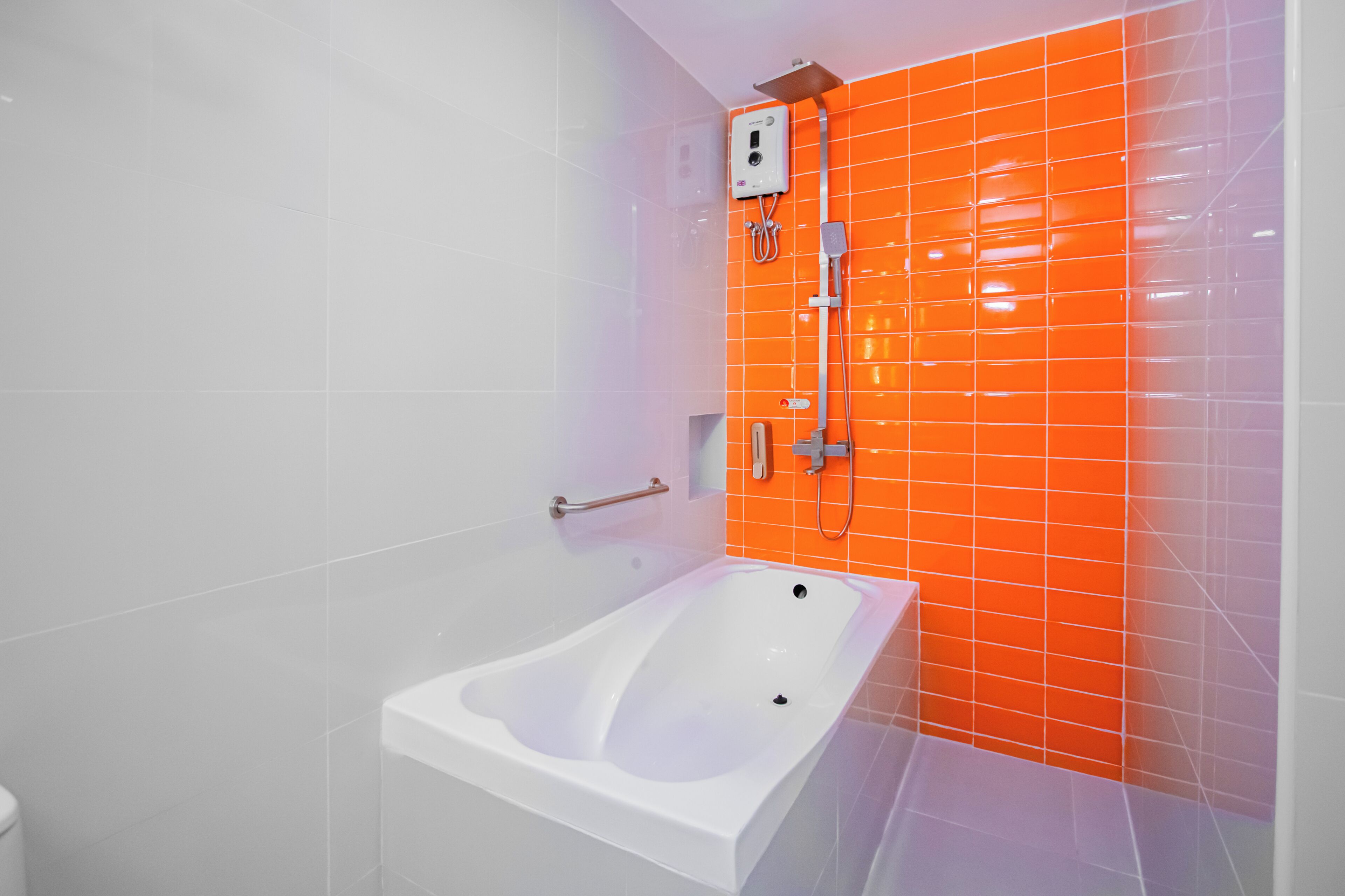 Une salle de bain avec une baignoire blanche, un mur recouvert de carreaux orange et une douchette à main.