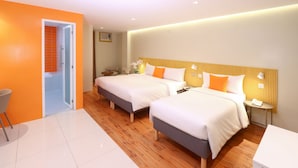 Habitación de hotel con dos camas, una mesita, una silla y un baño visible a través de una puerta abierta.