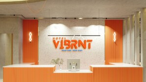 Un mostrador de recepción de diseño moderno, un letrero que dice 'HOTEL VIBRNT' y una planta en el centro.
