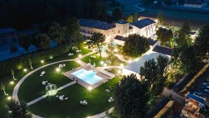 An aerial view of a hotel with a swimming pool, lounge areas, and a well-lit garden.