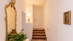 A hallway with a staircase, a mirror, a wall-mounted lamp, a door, and a framed picture.