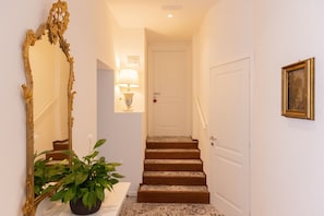 A hallway with a staircase, a mirror, a wall-mounted lamp, a door, and a framed picture.
