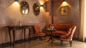 A room with a patterned wall, a sofa, two chairs, a small table with a candle, and wall-mounted lights.