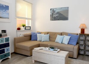 A living room with a beige sofa, a white wicker coffee table, a lamp, and a framed picture on the wall.