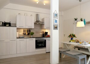 A modern kitchen with light wood cabinets, a stainless steel range hood, and a built-in oven.